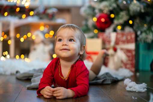 Portrait of cute happy little girl lying on the floor against Christmas tree at home