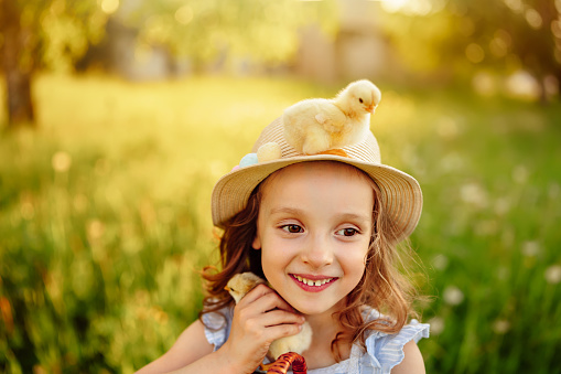 A girl with a small chicks in her hands. A little chicken on the hat of a happy girl. Egg and chicken are a symbol of life. Happy Easter Holiday Wishes