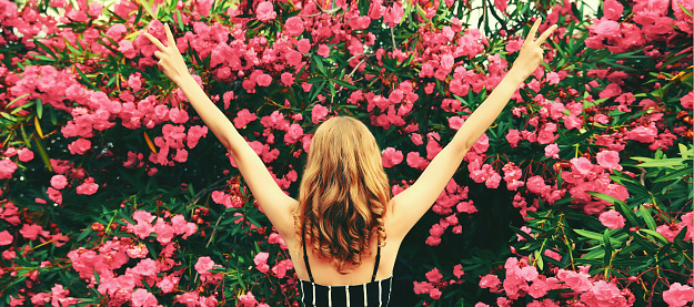 Beautiful happy woman raising her hands up in garden on roses flowers background, back view