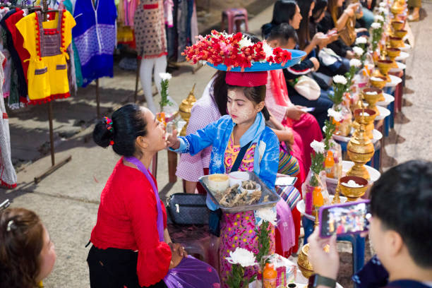 la pequeña mujer tailandesa mon con una bandeja de flores en la cabeza está dando sellos de flores en las mejillas de las mujeres tailandesas que esperan en la ceremonia del día de makha bucha - sangkhlaburi fotografías e imágenes de stock