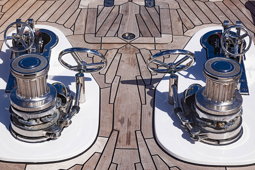 Teak deck of a luxury yacht with stainless steel winches and anchor chain attachment mechanisms.