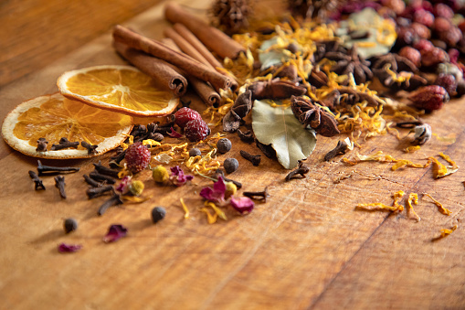 A variety of spices and petals including cloves, star anise, bay leaves, cinnamon, allspice, rose petals, calendula petals, rose hips, and dried orange slices thrown on a rustic cutting board.