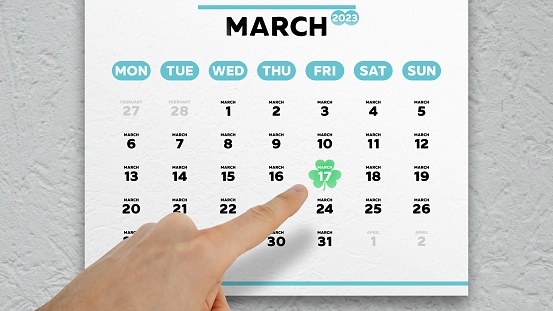 A male hand points finger to Saint Patrick’s Day on a March page of the wall calendar 2023