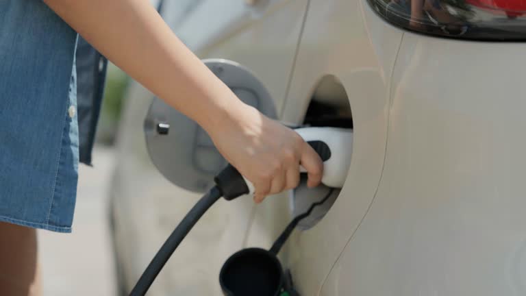 Asian woman is opening the car hood to refuel his electric car.