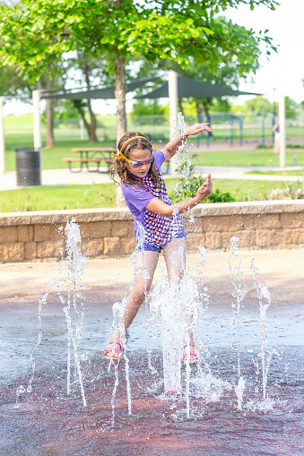 Young girl dancing with the water fountains at a splash pad on a summer day.