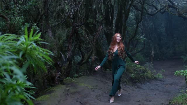 Beautiful woman in an elf costume is walking in a magic green enchanted forest.