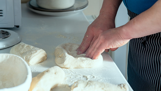 Chef Stretching and folding bread dough on top of white table with dusted flour side view.