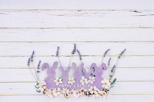 Flat lay of purple wooden vintage easter bunny shapes with lavender, almond blossoms and purple English lettering Happy Easter and copy space around. Color editing with added grain. Very selective and soft focus. Part of a series.