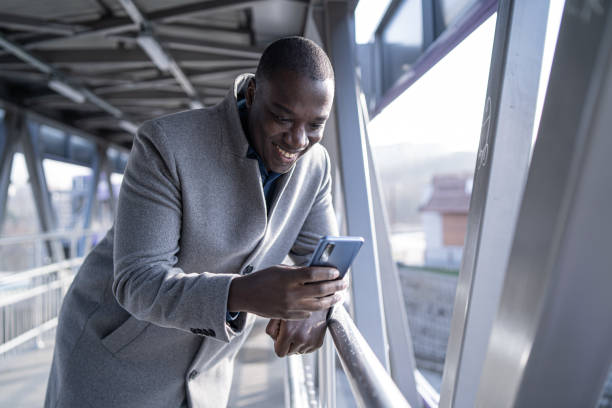 istock Smiling african-american man, messaging and surfing the net on his mobile, while standing under a pedestrian bridge 1471942357
