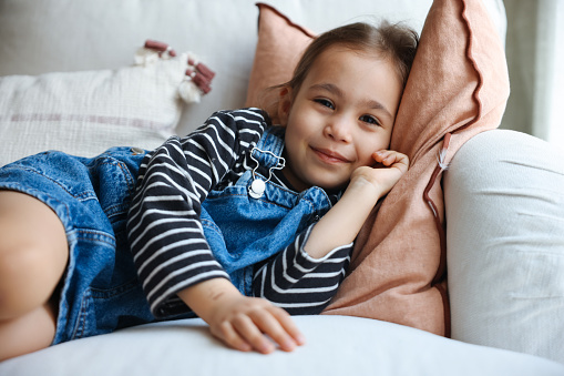 Cheerful girl lies on couch hugging a pillow and smiling. Happy child kid resting at home