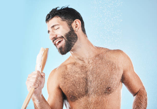 doccia, canto e pulizia con un modello di uomo in studio su uno sfondo blu usando una luffa per cantare. acqua, bagno e igiene con un bel maschio bagnato durante il lavaggio per la cura personale del corpo - male men body fashion model foto e immagini stock