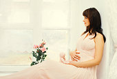 Portrait of beautiful young pregnant dreaming woman with teddy bear toy in home
