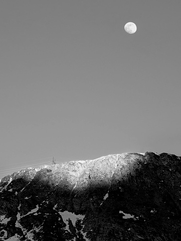 Luna e ultimi raggi di sole illuminano la roccia della montagna