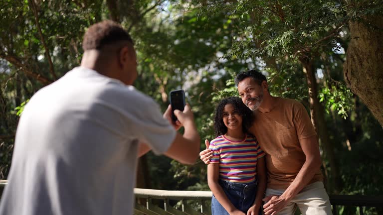 Gay couple with their daughter filming using mobile phone in the park