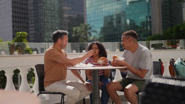 Homosexual family eating hamburger outdoors