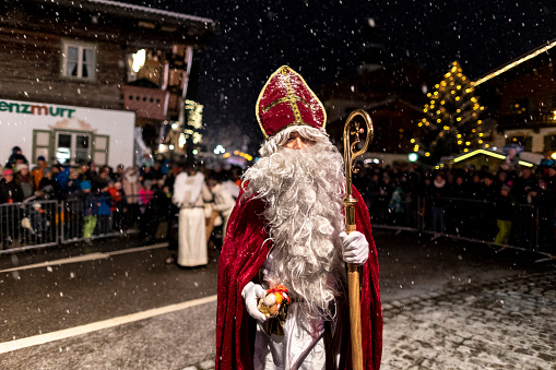 Reit im Winkl, Bavaria, Germany, December 2022, event with differnt  traditional groups , alpin christmas tradition Perchten Run, facial portrait of Saint Nicholas with his white beard, walking towards the camera in a red cape, a large crowd of visitors in the background