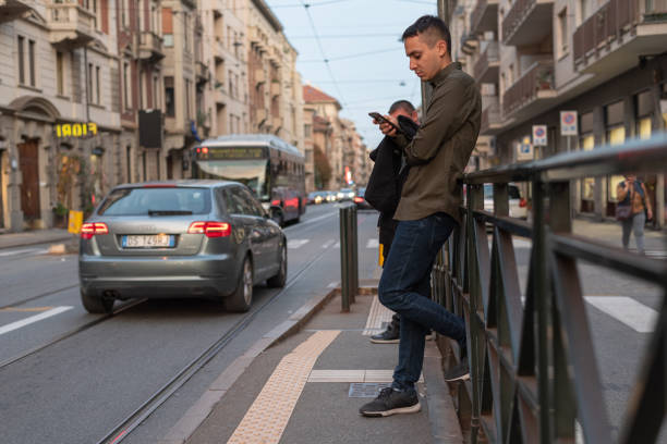 giovane che guarda il suo cellulare mentre aspetta il tram - autobus italy foto e immagini stock