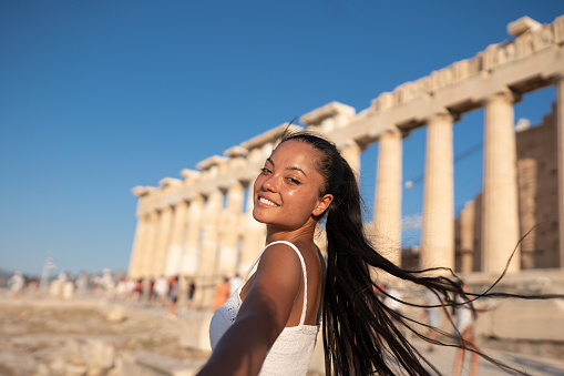 Follow me to Acropolis in Athens, Greece. Smiling female asian tourist leading boyfriend to the magnificent famous Parthenon. People travel concept