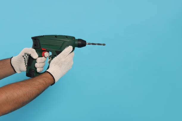 istock Worker in gloves with power drill on light blue background, closeup. Space for text 1471960033