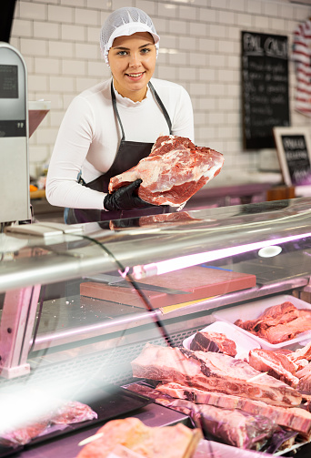 Smiling female butcher offering to sell big piece of beef in butcher shop