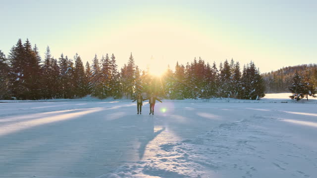 AERIAL Two people holding hands and skating on a frozen lake