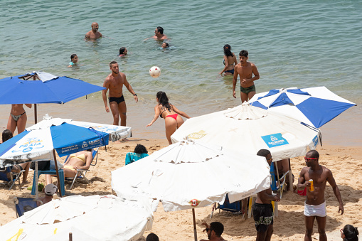 Salvador, Bahia, Brazil - January 14, 2022: People and tourists are playing beach soccer on Porto da Barra beach under strong summer sun. Salvador, Bahia.