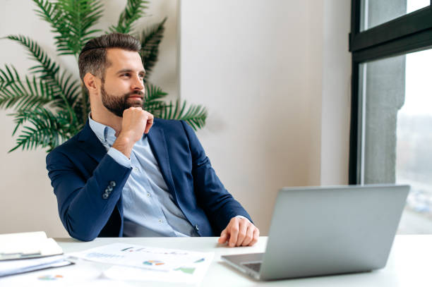 istock Pensive dreamy caucasian attractive successful businessman, sit at work desk, taking break from work, looking out the window, dreaming about vacation, thinking about a new project, planning a strategy 1471974225