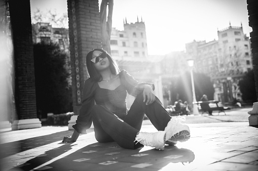 A beautiful young African woman in a park, lifestyle. Fashionably posed, sitting on the floor in black and white