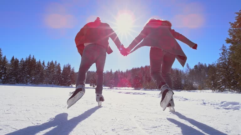 SLO MO TS Man and woman holding hands and ice skating on the frozen lake in sunshine