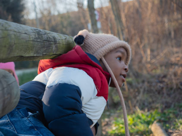 portrait of african kid sta ding outdoors in a park a sunny day wearing winter garment and a beanie hat with earflaps
