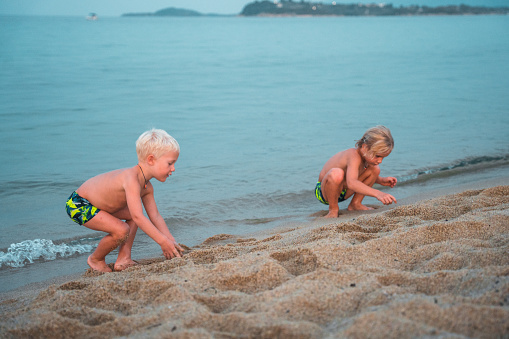 Cute young brothers playing on the sand at the beach. They are wearing swimwear on a relaxing summer afternoon. They are on a family vacation.