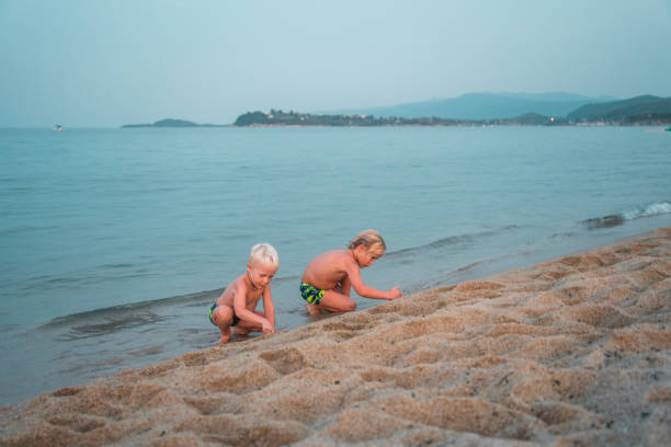 Happy young children digging in the sand, playing and enjoying time together. They are two caucasian brothers on a family holiday.