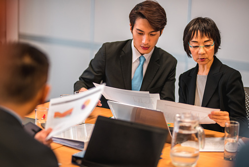 Group of Asian businessman wearing suits talking using digital tablet together while standing in conference room. Two asian businessman discussing ideas concept. business, people