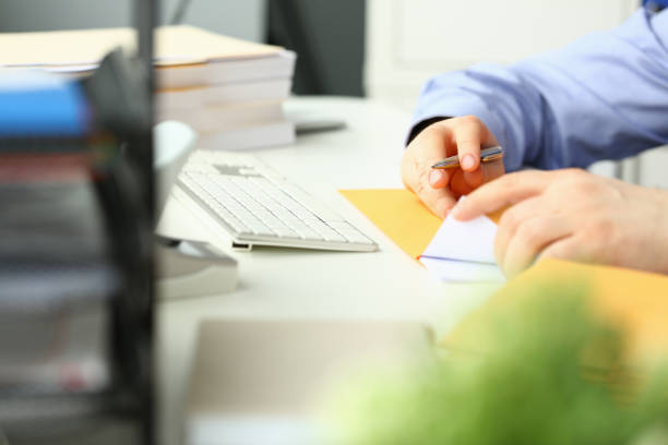 Businessman is sitting at table in office holding yellow envelope and taking out sheet of notification of a received paper letter closeup Businessman is sitting at table in office holding yellow envelope and taking out sheet of notification of a received paper letter closeup. Business correspondence corporate news and notice gun laws stock pictures, royalty-free photos & images