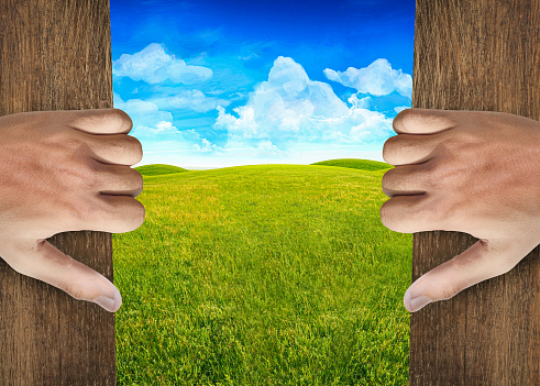 Hands open door into green field background