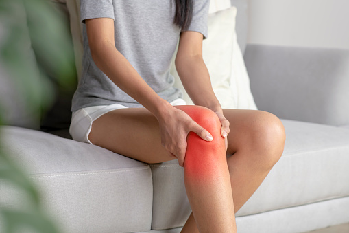 A young woman massaging her painful knee marked with red spot.