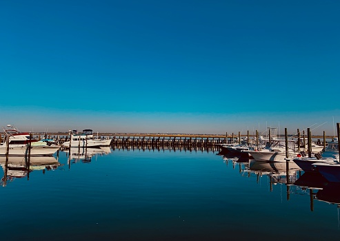 Boat marina in Long Island with boats docked and their reflection in bright blue waters.