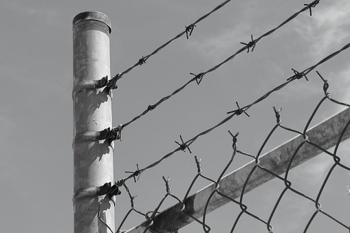 A barbed wire fence placed over a wire fence.   Black and white photography