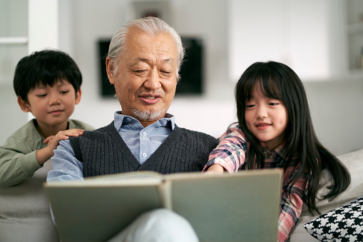senior asian grandfather having a good time with two grandchildren at home