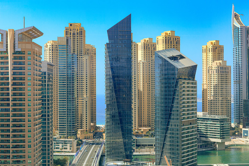 Dubai, United Arab Emirates - High angle view across Sheikh Zayed Road and Dubai Marina, towards the tall sand coloured towers of The Jumeirah Beach Residence. In the far background in between the towers can be seen the waters of the Persian Gulf. Image shot in the morning sunlight from a Jumeirah Lake tower on the opposite side. Horizontal format.