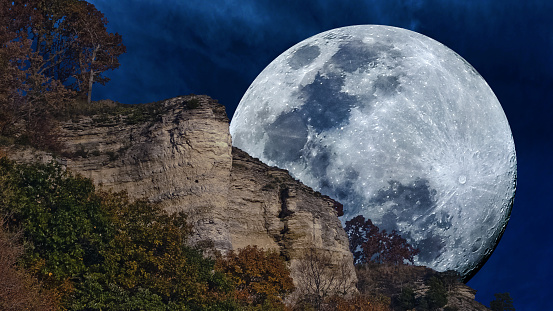 Close-up artistic photo of a full moon partially obscured by a stone bluff formation and rocky cliffs. Copy space.