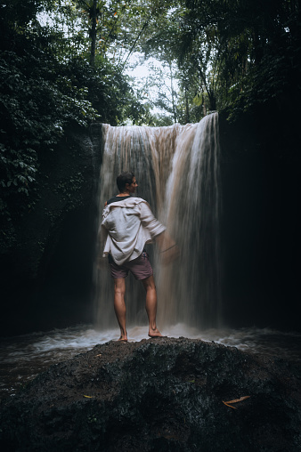 Walks in the tropical jungle and looks at a strong waterfall. Adventure, tourism, exploration and travel. Tropical forest and waterfall.