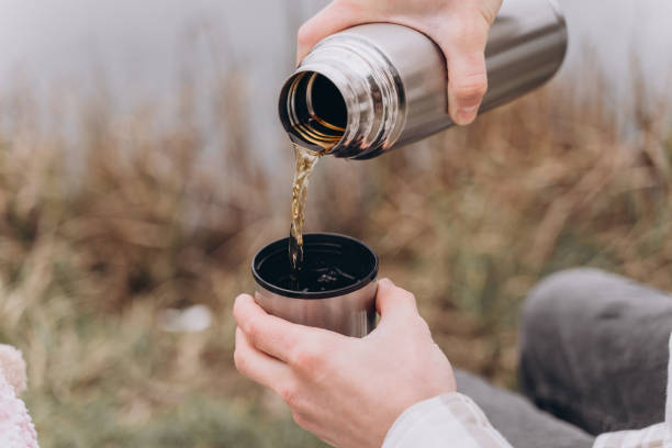 istock Hot tea is poured from a thermos into a cup in nature, close-up 1472003309