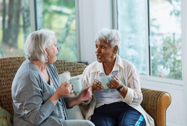 istock Two senior women conversing on sofa, with coffee 1472003320