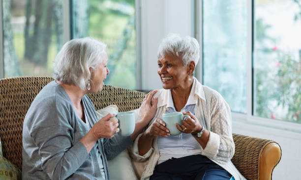 istock Two senior women conversing on sofa, with coffee 1472003322