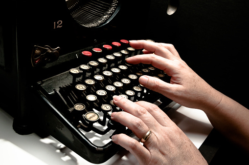Woman's hands typing on a antique typewriter, interesting piece, mix of art, culture and historical engineering.