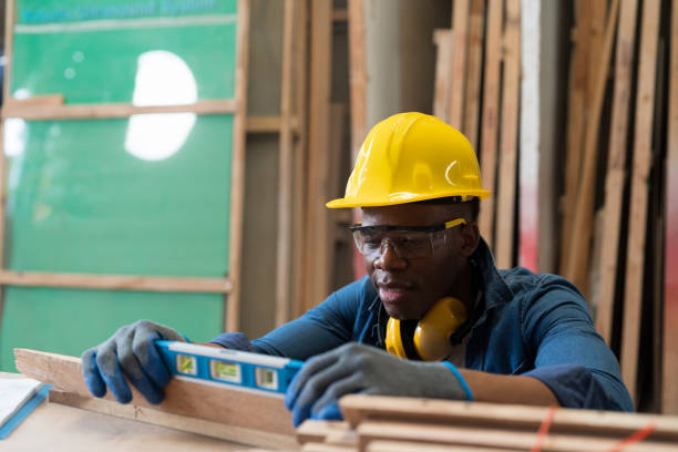istock Male carpenter using water level in wood processing plants. Black male carpenter working at wood workshop. Young man carpenter wearing safety equipment and working in furniture workshop 1472006555