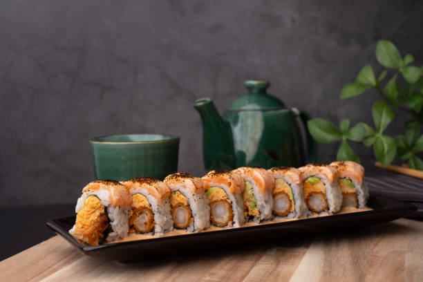 tempura sushi roll topped with seared salmon and serve with hot tea. japanese traditional dishes and healthy food. - sushischotel stockfoto's en -beelden