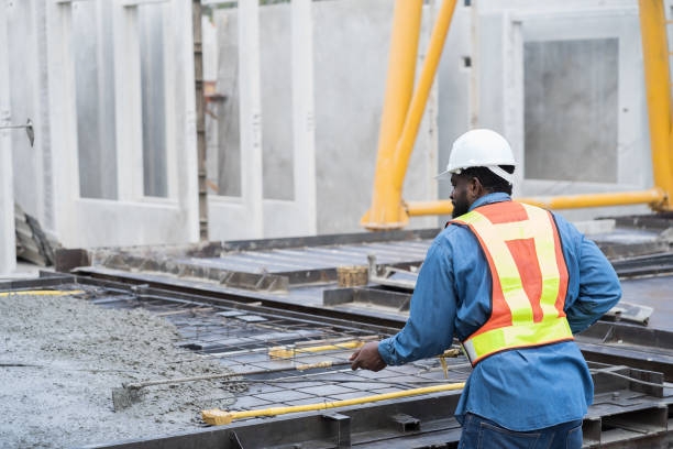 Construction worker uses long steel trowel spreading wet concrete pouring at precast concrete wall construction site. Worker or mason working or making smooth surface of concrete with equipment tool trabajador de la construcción utiliza paleta de acero larga que extiende el concreto húmedo vertiendo en el sitio de construcción de muros de concreto prefabricados. trabajador o albañil trabajando o haciendo superficie lisa de concreto con herramienta