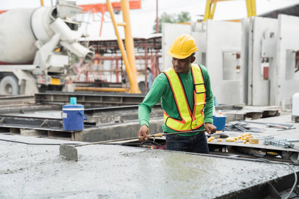 istock Construction worker uses long steel trowel spreading wet concrete pouring at precast concrete wall construction site. Construction technician working by leveling concrete floor to smooth 1472008913